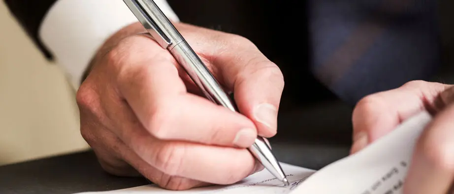 Hand som skriver på under ett dokument.